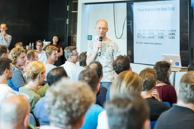 Lukas speaking while standing in the middle of a seated crowd at a Booking Data Science Meetup in Amsterdam, 2017.
