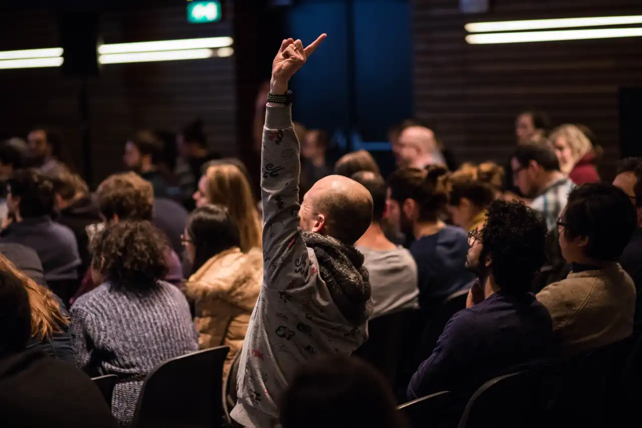 Lukas sitting in the crows raising his hand high to ask a question at a Booking Data Science Conference in Amsterdam, 2018.